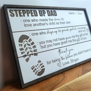 May include: A wooden sign with the text "Stepped Up Dad" and a message about the importance of being a stepparent. The sign features two footprints and the text "name | Dean" and "Love, Morgan".