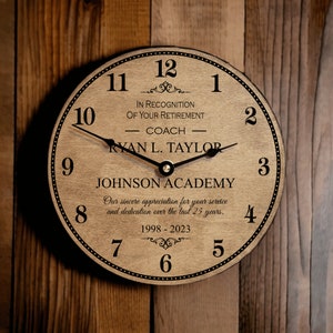 May include: A wooden clock with black hands and numbers. The clock face reads "In recognition of your retirement - Coach Ryan L. Taylor - Johnson Academy - Our sincere appreciation for your service and dedication over the last 25 years. 1998-2023".