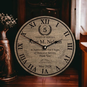May include: A wooden clock with Roman numerals and a black clock hand. The clock face has a laurel wreath with the number 5 in the center, the text "YEARS OF SERVICE", "Alan M. Nelson", "In Appreciation For 5 Years of Dedicated Service. Thank You.", "HARMONY", and "May 2024".