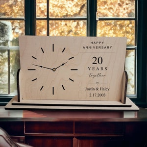 May include: A wooden anniversary clock with a light wood finish. The clock face features black hour markers and hands. The text "HAPPY ANNIVERSARY 20 YEARS together" is printed above the names "Justin & Haley" and the date "2.17.2003".