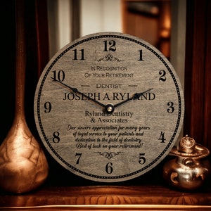 May include: A wooden clock with a gray background and black hands. The clock face has a message that reads "In recognition of your retirement - Dentist - Joseph Aryland - Ryland Dentistry & Associates - Our sincere appreciation for many years of loyal service to your patients and dedication to the field of dentistry. Best of luck on your retirement!"