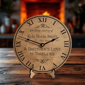 May include: A wooden clock with black Roman numerals and hands. The clock face includes the text "In loving memory of Kyle Merin Smith" and "A Brother's Love Is Timeless". The clock is displayed on a wooden stand.