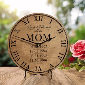 May include: A wooden clock with Roman numerals and a stand. The clock face is brown with black text that reads "My greatest blessings call me MOM" and lists dates and names.
