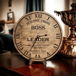 May include: A wooden clock with Roman numerals and a quote about leadership. The quote reads "It's one thing to be a boss, another thing to be a mentor, but a completely different thing to be a leader." The clock also includes the text "We are lucky to have been led by a boss, mentor & leader like you." The clock is personalized with the name "Derrick A. Pace" and the date "September 22, 2023".