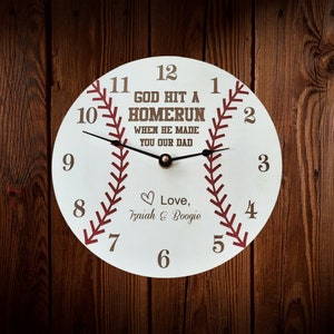 May include: White baseball-themed clock with brown numbers and red stitching. The clock face reads "God hit a homerun when he made you our dad." and "Love, Isaiah & Boogie".