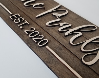 May include: A wooden sign with the words "the johns" in white script and "EST. 2020" below in white lettering.