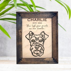 May include: A wooden framed memorial plaque with a laser-cut silhouette of a dog's head. The plaque reads "CHARLIE 2016-2024 You left paw prints on our hearts..."