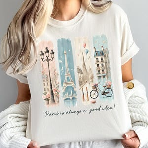 May include: A white t-shirt with a graphic print of a Parisian cityscape, including the Eiffel Tower, a bicycle, and streetlights. The text "Paris is always a good idea!" is printed below the graphic.