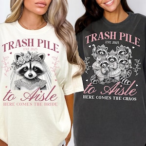 May include: Ivory and pepper-colored t-shirts with raccoon graphics. The ivory shirt features a raccoon bride with text "Trash Pile to Aisle, Here Comes the Bride, Est. 2025." The pepper shirt shows raccoons with text "Trash Pile to Aisle, Here Comes the Chaos, Est. 2025."