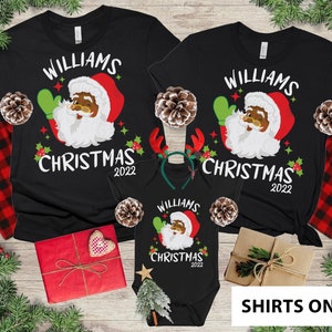 May include: Black Christmas shirts with a cartoon Santa Claus wearing a green hat and holding a green mitten. The shirts say "Williams Christmas 2022".