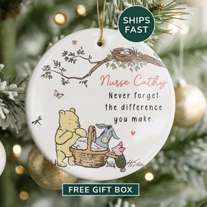 May include: A white ceramic Christmas ornament with a gold string for hanging. The ornament features a Winnie the Pooh theme with the text "Nurse Cathy, Never forget the difference you make."