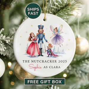 May include: Round white Christmas ornament featuring a Nutcracker theme. The ornament has a painted illustration of characters from the ballet, including a Nutcracker, Clara, a fairy, and a mouse king. Text includes "The Nutcracker 2025" and "Sophie as Clara."