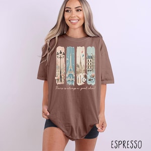 May include: A brown oversized t-shirt with a graphic print of Parisian landmarks and the text "Paris is always a good idea!"