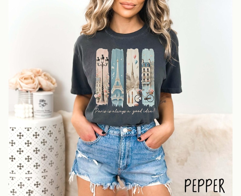 May include: A dark gray t-shirt with a graphic print of a Parisian cityscape, including the Eiffel Tower, a bicycle, and streetlights. The text "Paris is always a good idea!" is printed below the graphic.