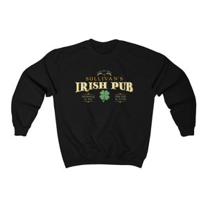Puede incluir: Sudadera negra con un gr&aacute;fico dorado y verde que dice "Sullivan's Irish Pub" con tr&eacute;boles y el texto "Whiskey & Ale" y "Friends & Food".