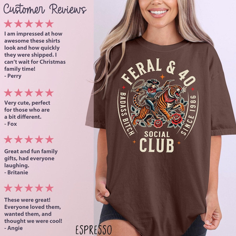 May include: Espresso-colored t-shirt featuring a graphic of a woman riding a tiger, with the text "FERAL & 40" and "BADASS BITCH SOCIAL CLUB SINCE 1986". The shirt has a crew neck and short sleeves.