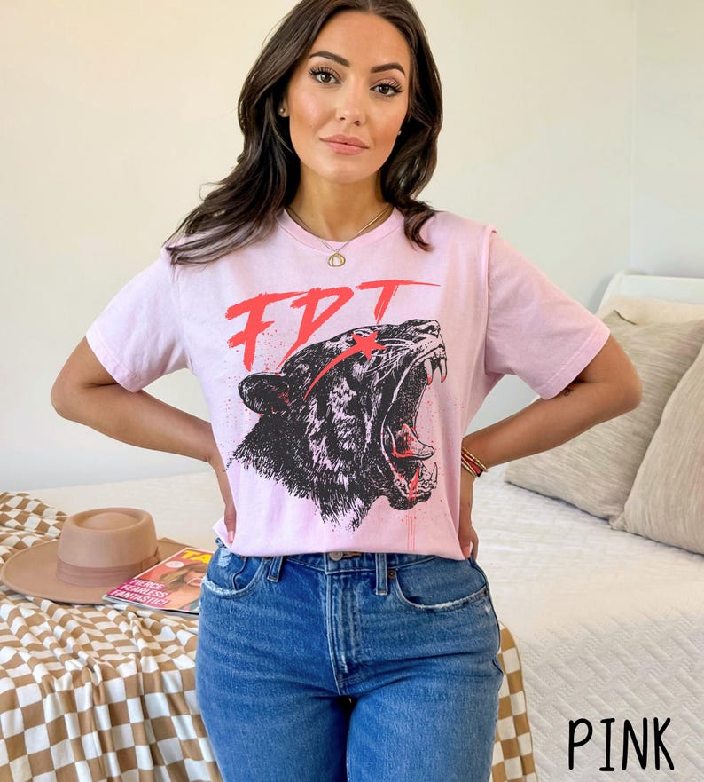 Peut inclure: T-shirt rose avec un motif noir et blanc d'un tigre rugissant avec des accents rouges. Le motif comprend le texte "FDT".