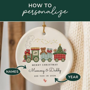 May include: A round, white Christmas ornament featuring a festive train design. The train cars are decorated with a teddy bear, gifts, and a Christmas tree. The ornament includes the text "Merry Christmas Mommy & Daddy" and "See you in 2026".