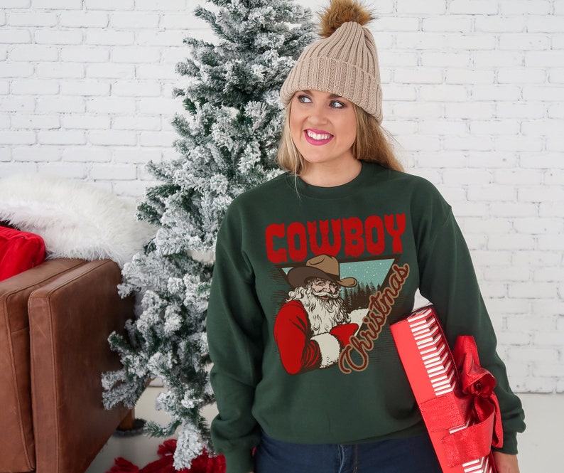 May include: A green Christmas sweater with a vintage illustration of Santa Claus wearing a cowboy hat and the text "Cowboy Christmas".