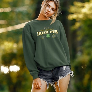 Puede incluir: Una sudadera verde oscuro con un gr&aacute;fico dorado y verde que dice "Sullivan's Irish Pub" con un tr&eacute;bol y el texto "Whiskey & Ale" y "Friends & Food".