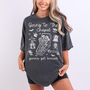 May include: Dark gray t-shirt with the phrase "Going to The Chapel gonna get buried" in white. The shirt features a coffin with skeletons, a church, bats, and other gothic-themed illustrations.