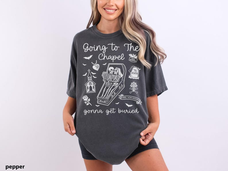May include: Dark gray t-shirt with the phrase "Going to The Chapel gonna get buried" in white. The shirt features a coffin with skeletons, a church, bats, and other gothic-themed illustrations.