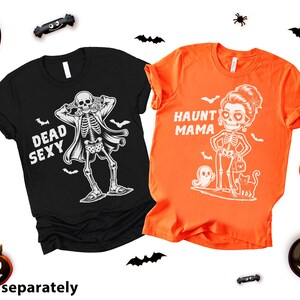 K&ouml;nnte beinhalten: Zwei Halloween-T-Shirts. Ein schwarzes Shirt mit einem Skelett-Motiv und den Worten "DEAD SEXY". Das andere ist orange mit einem Skelett-Frauen-Motiv und den Worten "HAUNT MAMA". Halloween-Dekorationen umgeben die Shirts.