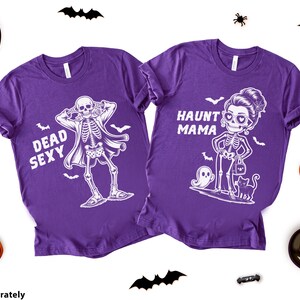 K&ouml;nnte beinhalten: Zwei lila T-Shirts mit Halloween-Skelett-Grafiken. Eines sagt "Dead Sexy" und zeigt ein Skelett in einem Mantel. Das andere sagt "Haunt Mama" und zeigt ein Skelett mit Handtasche und Katze. Halloween-Dekorationen umgeben die Shirts.