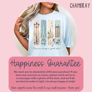 May include: A light blue t-shirt with a graphic print of a Parisian cityscape, including the Eiffel Tower, a bicycle, and a street lamp. The text "Paris is always a good idea!" is printed below the graphic. The shirt is on a pink background.