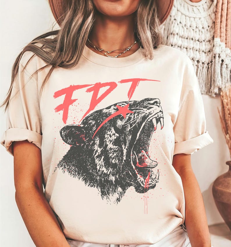 Peut inclure: Un t-shirt beige avec un motif noir et blanc d'un tigre rugissant avec une &eacute;toile rouge sur le front. Le texte "FDT" est &eacute;crit en rouge au-dessus du tigre.