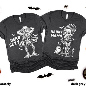 K&ouml;nnte beinhalten: Zwei dunkelgraue Heather-T-Shirts mit Halloween-Motiven. Eines zeigt ein Skelett und den Text "Dead Sexy". Das andere sagt "Haunt Mama" mit einer Skelettfrau, einem Geist und einer Katze. Halloween-Dekorationen umgeben die Shirts.