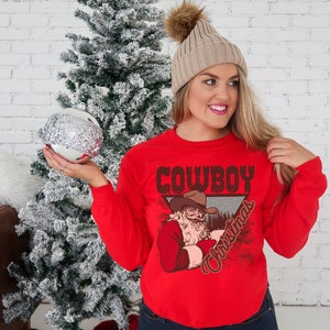 May include: Red long-sleeved sweatshirt with a vintage-style graphic of a cowboy Santa Claus with the text "Cowboy Christmas".