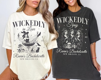 May include: Two oversized t-shirts, one ivory and one pepper, with witch-themed graphics. The ivory shirt says "Wicked in Love" with a witch illustration. The pepper shirt says "Wickedly Tipsy" with a group of witches. Both shirts say "Raven's Bachelorette, New Orleans, LA."