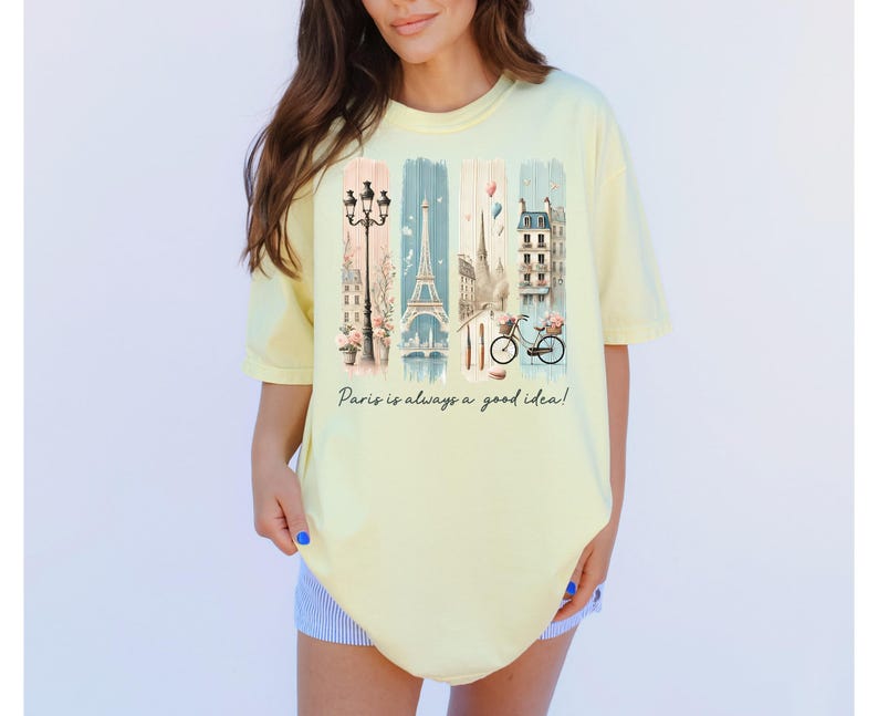 May include: A yellow t-shirt with a graphic print of a Parisian street scene, including the Eiffel Tower, a bicycle, and a street lamp. The text "Paris is always a good idea!" is printed below the graphic.