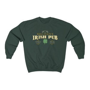 Puede incluir: Una sudadera de color verde oscuro con un dise&ntilde;o gr&aacute;fico dorado y blanco que dice "Sullivan's Irish Pub" con tr&eacute;boles y el texto "Whiskey & Ale" y "Friends & Food".