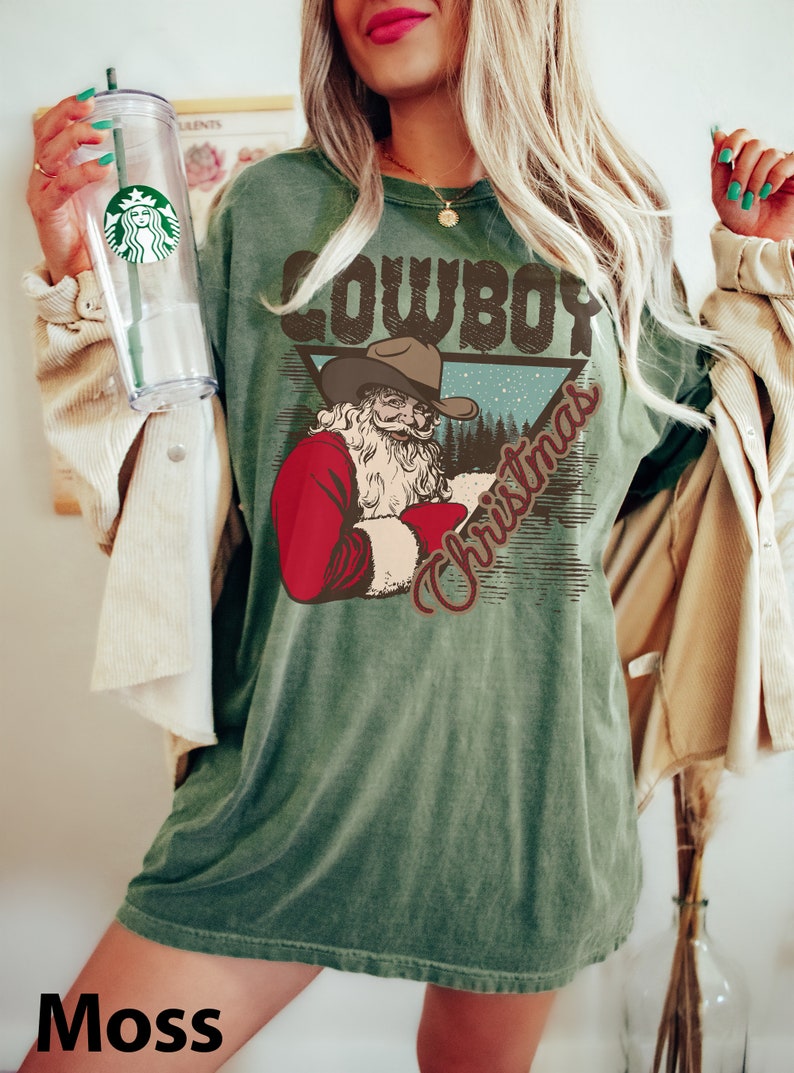 May include: Green t-shirt with a vintage-style graphic of a cowboy Santa Claus with the text "Cowboy Christmas".