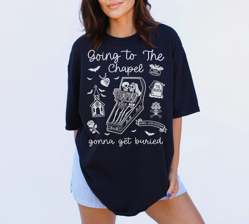 May include: Black t-shirt with a white graphic featuring skeletons in a coffin, a church, and the text "Going to The Chapel gonna get buried." The design includes bats, a rose, and a tombstone.