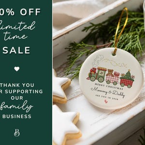 May include: A white ceramic Christmas ornament with a train design, featuring a teddy bear and Christmas tree. The ornament has the text "Merry Christmas Mommy & Daddy See You in 2026". The image also includes star-shaped cookies and text that says "50% OFF limited time SALE".