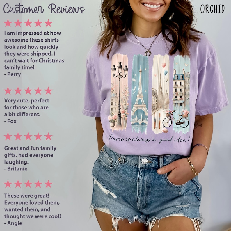 May include: Purple t-shirt with a graphic print of a Parisian street scene, including the Eiffel Tower, a bicycle, and a street lamp. The text "Paris is always a good idea!" is printed on the shirt.