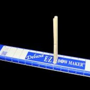 May include: A blue and white Deluxe EZ Bow Maker with two wooden dowels inserted. The bow maker has a ruler printed on it and the words "Deluxe EZ Bow Maker".