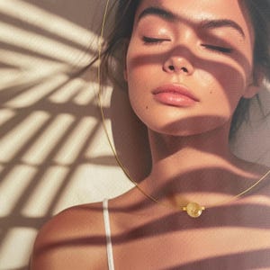 Puede incluir: Primer plano de la cara de una mujer con los ojos cerrados. Lleva un collar de oro con un colgante redondo amarillo. El fondo es beige claro con sombras.