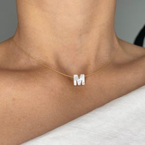 May include: A gold chain necklace with a white pearl letter M pendant.