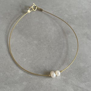 Op de afbeelding: Een delicate gouden kettingarmband met twee kleine witte parels.