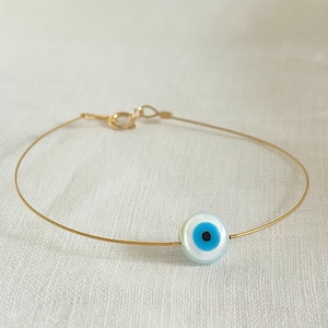 Op de afbeelding: Een gouden kettingarmband met een blauwe en witte boze oog bedel.
