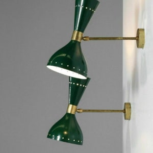 May include: Two green wall sconces with brass accents. Each sconce has a double-cone shade with small, evenly spaced holes. The sconces are mounted on a wall with brass arms and circular wall plates. The shades are dark green.