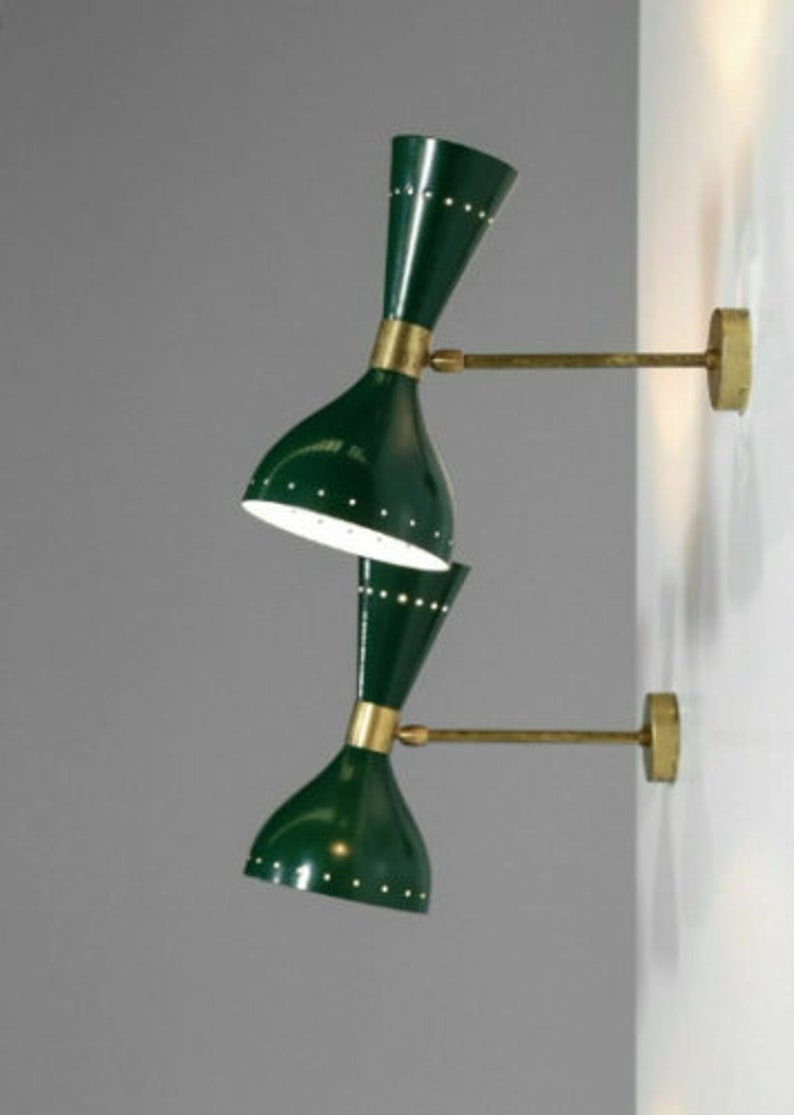 May include: Two green wall sconces with brass accents. Each sconce has a double-cone shade with small, evenly spaced holes. The sconces are mounted on a wall with brass arms and circular wall plates. The shades are dark green.
