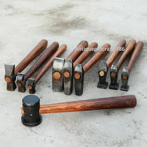 May include: A set of ten antique wooden-handled hammers with metal heads. The hammers are arranged in a row on a grey surface. The hammers are all different sizes and shapes. The hammers are used for various tasks, such as shaping metal, driving nails, and breaking rocks.