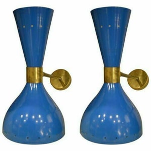 May include: Two blue wall sconces with brass accents. Each sconce has a flared base and a conical top, connected by a brass band. The sconces have small, evenly spaced holes and are mounted on round brass wall plates.
