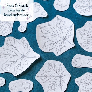 May include: A collection of white Stick & Stitch patches for hand embroidery featuring various sizes of maple leaf outlines printed in black ink, scattered across a solid teal fabric background with a clear, legible text overlay.