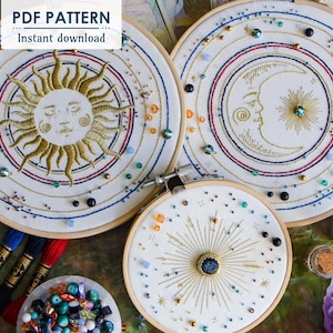 May include: Three embroidery hoops with celestial designs. The hoops are white with gold embroidery of a sun, moon, and a starburst. The designs are surrounded by colorful beads.